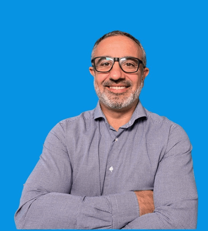 Person in a collared shirt standing against a blue background with arms crossed.