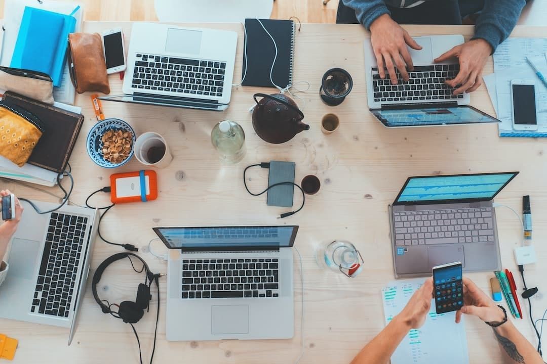 Top view of a collaborative workspace with laptops, notebooks, and drinks on a wooden table.