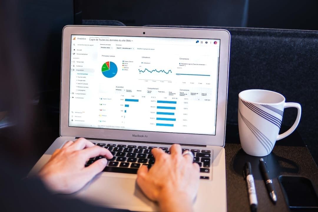 Person analyzing data charts on a laptop with a coffee cup and markers on the table.